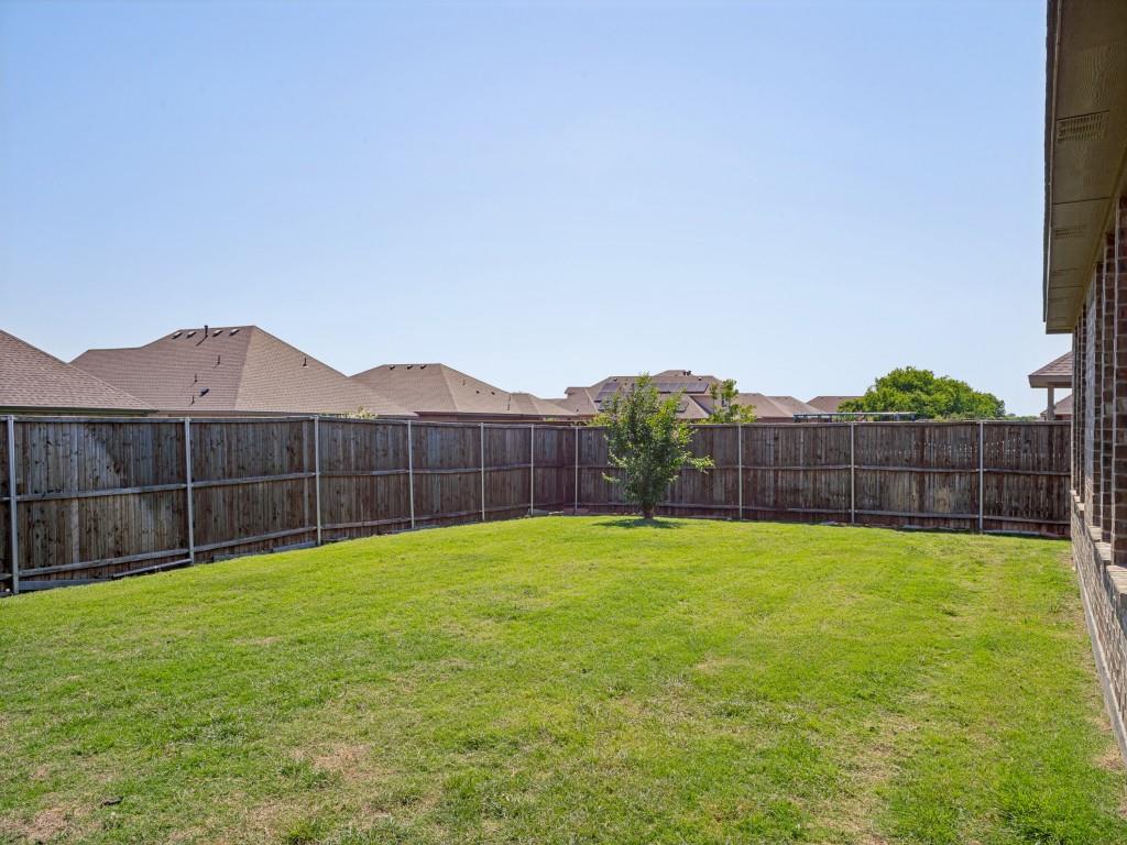 1612 Reed Drive Krum, TX 76249 - Photo 24 of 25 Expansive backyard with a manicured lawn, full privacy fencing, brick exterior wall, and a single mature tree