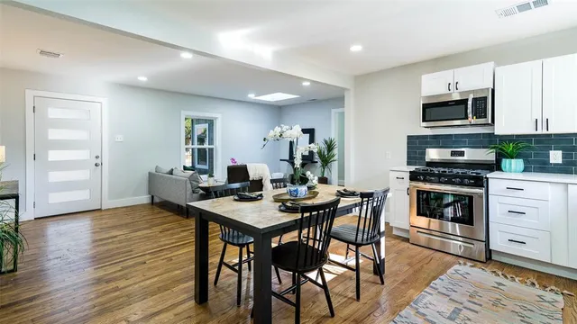 a kitchen with stainless steel appliances kitchen island granite countertop a stove top oven a sink dishwasher and a dining table with wooden floor