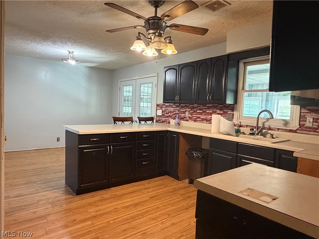 3950 Wolf Road Southwest Port Washington, OH 43837 - Photo 12 of 45 Kitchen featuring dark cabinetry, light countertops, wood-finish flooring, a red tile backsplash, and a ceiling fan with integrated lighting
