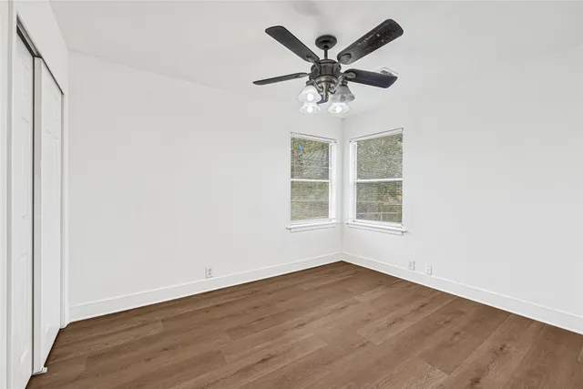 an empty room with wooden floor chandelier fan and windows