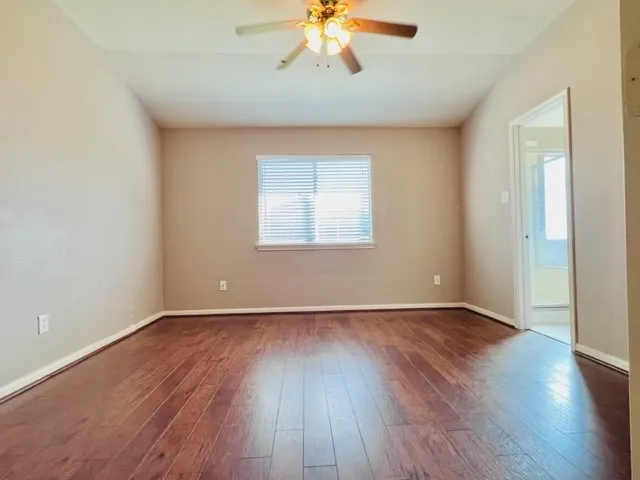 an empty room with wooden floor chandelier fan and windows