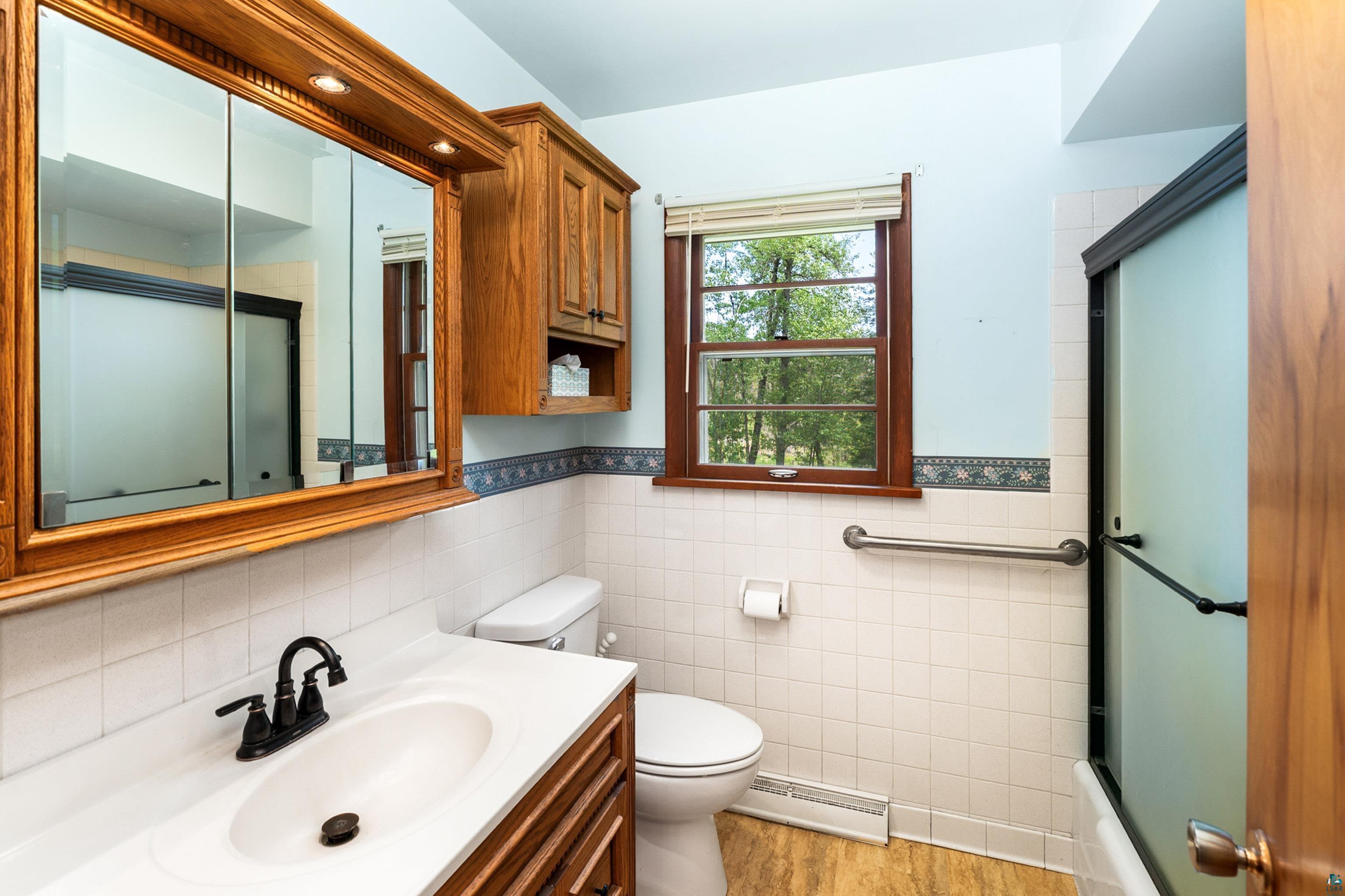 4808 Midway Road Duluth, MN 55811 - Photo 28 of 57 Bathroom featuring a light wood-finish vanity with a white countertop and oval sink, dark bronze faucet, and a large wood-framed mirrored medicine cabinet with integrated lighting