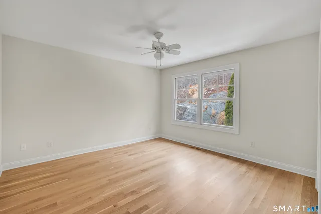 an empty room with wooden floor chandelier fan and windows