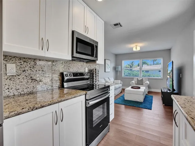 a kitchen with stainless steel appliances granite countertop a stove a sink dishwasher a microwave oven with white cabinets and wooden floor