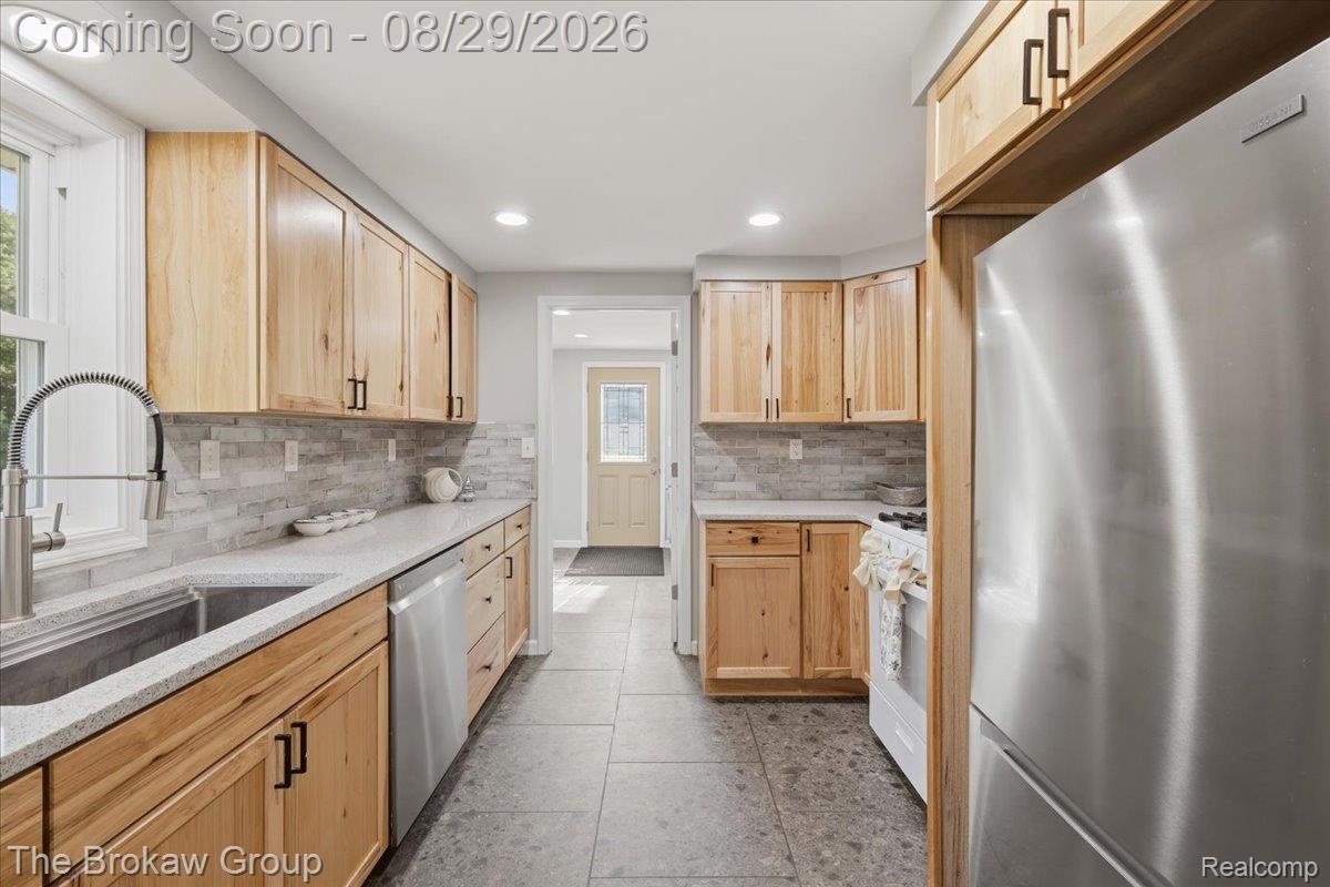 5411 Hess Road Dryden, MI 48428 - Photo 18 of 56 Galley kitchen featuring wood-finish cabinetry, stainless steel appliances, stone tile backsplash, and light-toned countertops