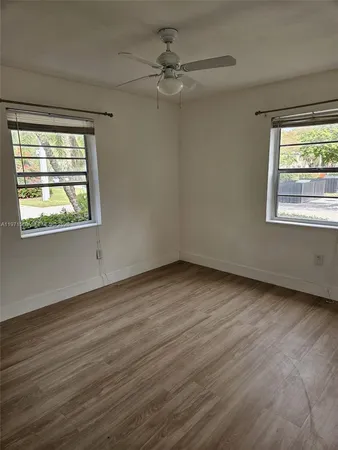 an empty room with wooden floor chandelier fan and windows