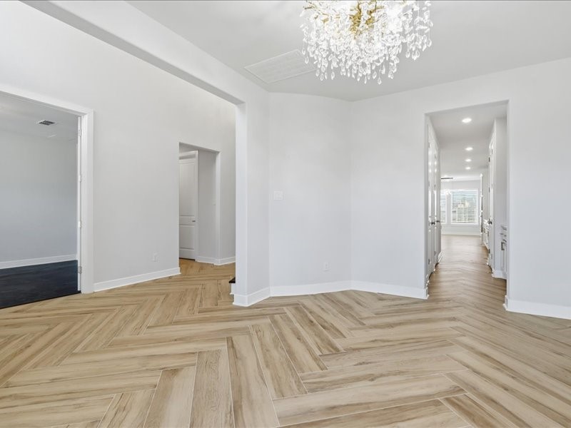 4710 Pecos Ridge Lane Sugar Land, TX 77479 - Photo 12 of 49 This photo showcases a bright, open hallway with elegant herringbone wood flooring and a modern crystal chandelier. The space features multiple doorways leading to different rooms, offering a spacious and inviting atmosphere.