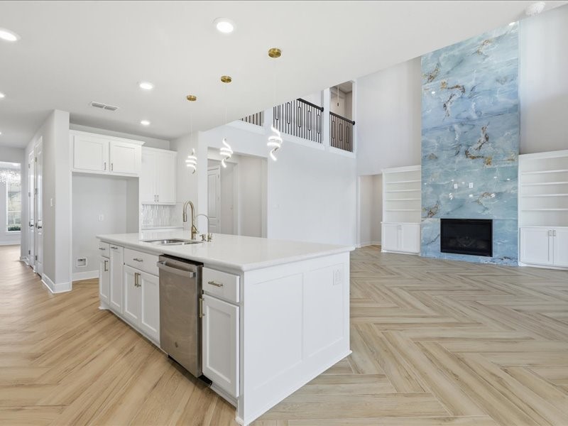 4710 Pecos Ridge Lane Sugar Land, TX 77479 - Photo 14 of 49 This modern open-concept living space features a spacious kitchen with a large island, elegant pendant lighting, and stainless steel appliances. Adjacent is a bright living area with a striking blue accent wall and built-in shelving flanking a cozy fireplace, all set on beautiful wood-patterned flooring.