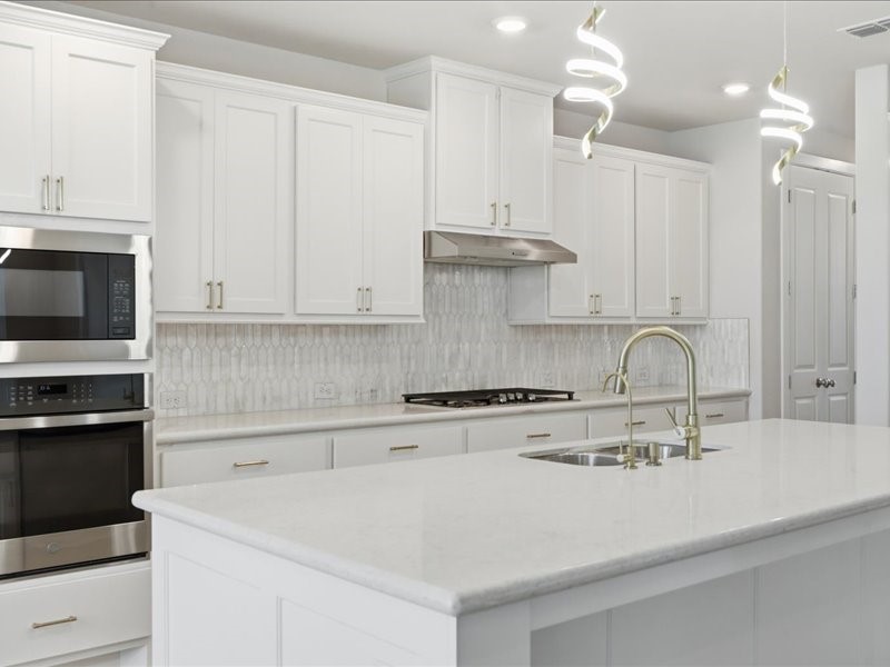 4710 Pecos Ridge Lane Sugar Land, TX 77479 - Photo 16 of 49 This modern kitchen features sleek white cabinetry, a spacious island with a built-in sink, and contemporary pendant lighting. It includes stainless steel appliances and a stylish backsplash, creating a bright and elegant space.