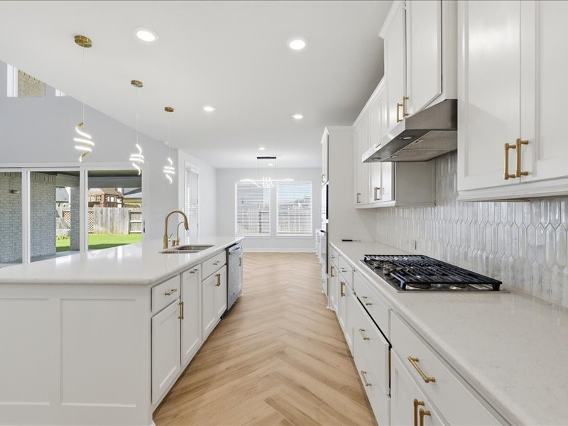4710 Pecos Ridge Lane Sugar Land, TX 77479 - Photo 17 of 49 This kitchen features sleek white cabinetry, modern pendant lighting, and a spacious island with a built-in sink. The light wood flooring complements the bright, airy atmosphere, enhanced by large windows and views of the backyard.