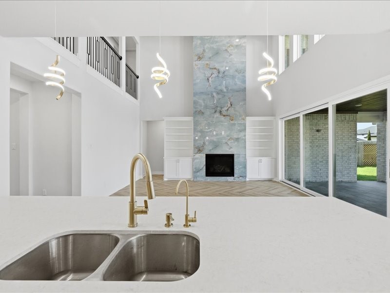 4710 Pecos Ridge Lane Sugar Land, TX 77479 - Photo 19 of 49 This modern living space features an open layout with high ceilings, a striking marble accent wall with a fireplace, and elegant spiral pendant lights. It includes a sleek kitchen island with a double sink and gold fixtures, and large sliding glass doors that lead to the outdoor area, providing plenty of natural light.