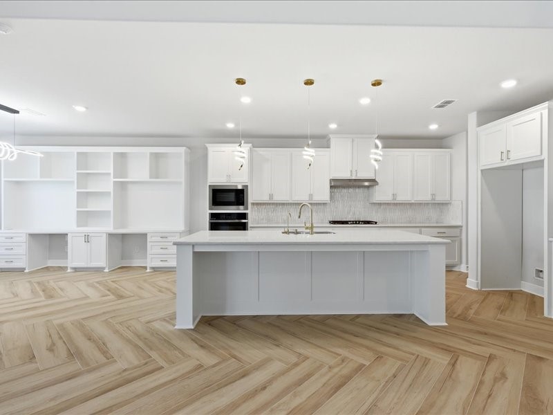 4710 Pecos Ridge Lane Sugar Land, TX 77479 - Photo 20 of 49 This modern kitchen features a spacious island with a sleek countertop, stylish pendant lighting, and ample cabinetry. The open layout includes a built-in oven, elegant backsplash, and a herringbone-patterned wooden floor, offering a bright and inviting space.