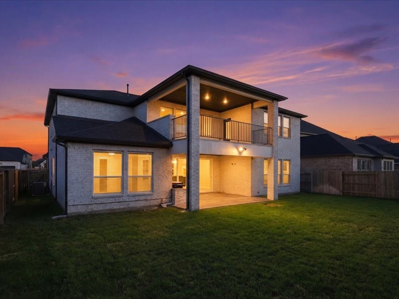 4710 Pecos Ridge Lane Sugar Land, TX 77479 - Photo 2 of 49 This two-story home features a spacious backyard with a covered patio and balcony, illuminated warmly against a stunning sunset backdrop.