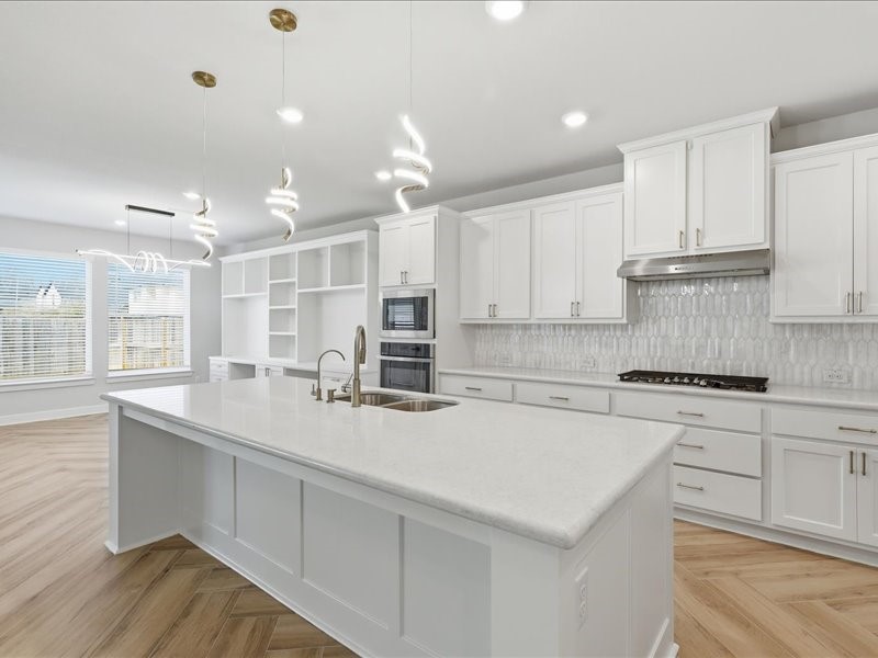 4710 Pecos Ridge Lane Sugar Land, TX 77479 - Photo 21 of 49 This modern kitchen features bright white cabinetry, a large island with a sink, and elegant pendant lighting. It includes built-in ovens, a gas cooktop, and ample storage. The open layout flows into a sunlit dining area with large windows and wood-patterned flooring.
