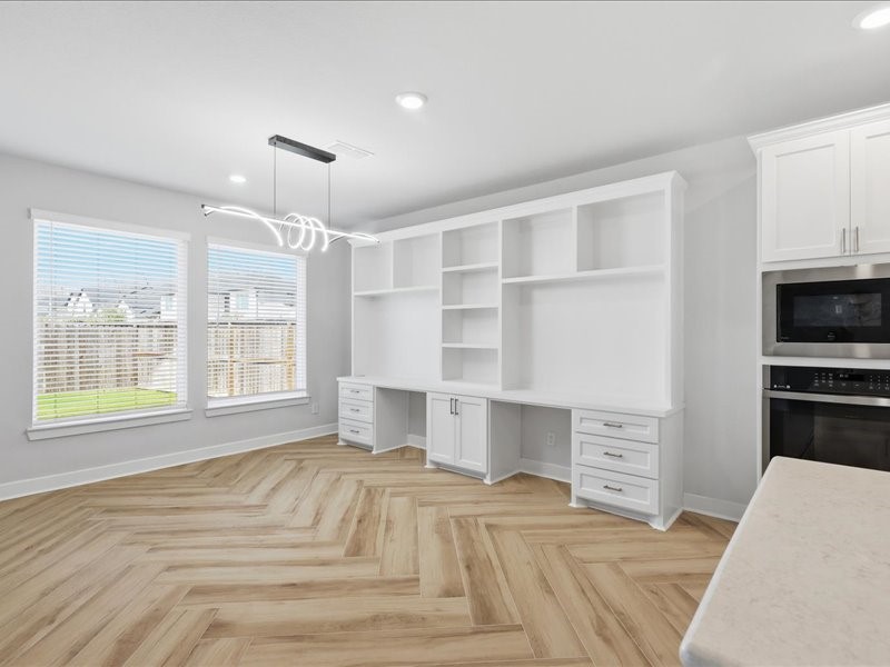 4710 Pecos Ridge Lane Sugar Land, TX 77479 - Photo 22 of 49 This space features a bright, open area with large windows, a modern light fixture, and built-in shelving and desk. The herringbone wood flooring adds elegance, and a contemporary kitchen area with an oven and microwave is visible.