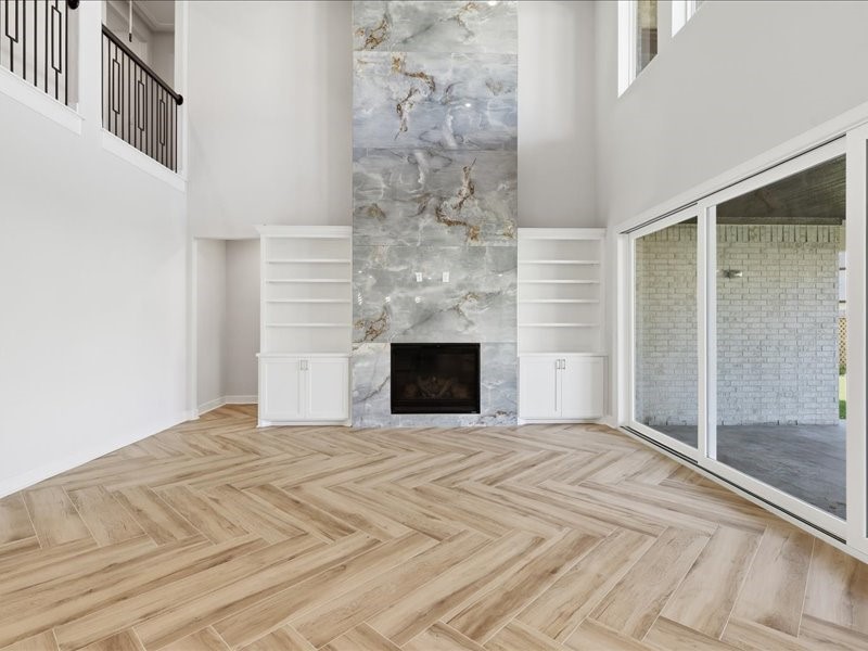 4710 Pecos Ridge Lane Sugar Land, TX 77479 - Photo 25 of 49 This spacious living room features a stunning floor-to-ceiling marble fireplace, elegant herringbone wood flooring, and abundant natural light from large sliding glass doors. Built-in shelves add functionality and style.