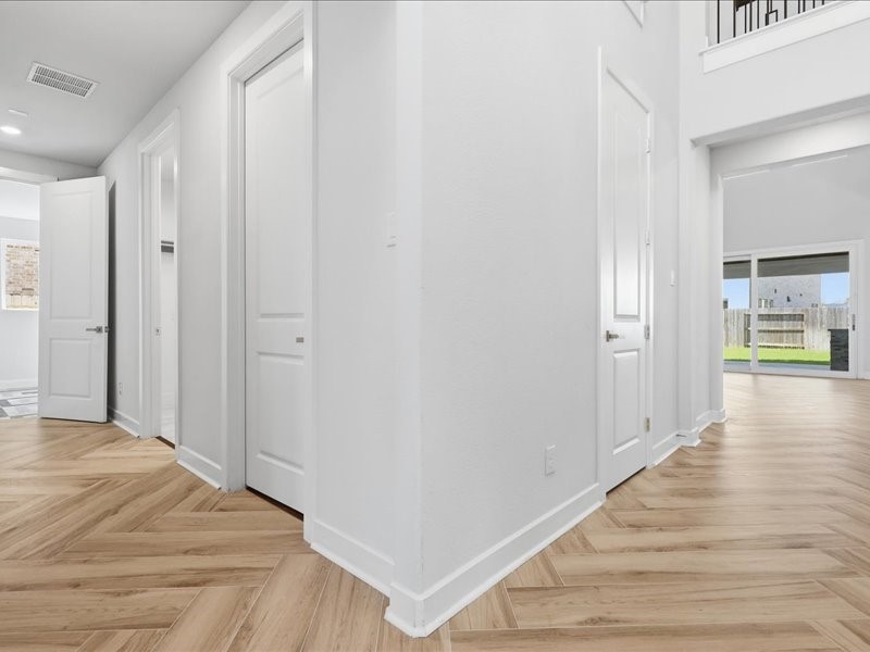 4710 Pecos Ridge Lane Sugar Land, TX 77479 - Photo 28 of 49 This photo showcases a bright hallway with elegant light wood herringbone flooring, white walls, and multiple doors leading to different rooms. The space opens up to a large area with sliding glass doors that provide a view of the backyard.