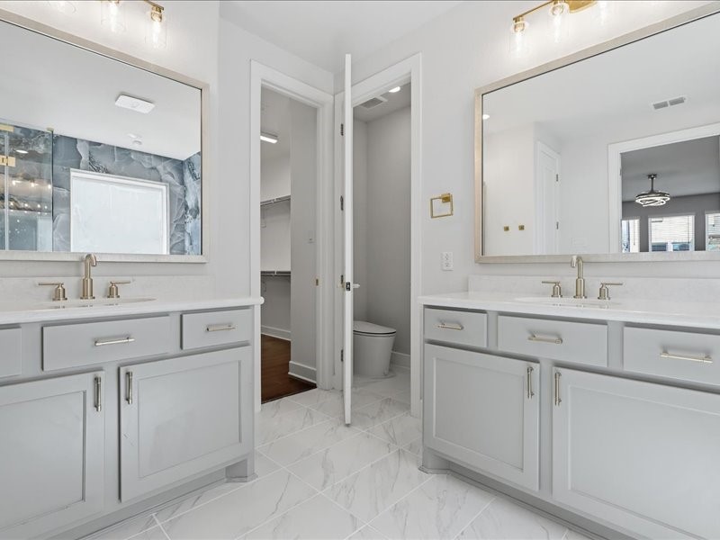 4710 Pecos Ridge Lane Sugar Land, TX 77479 - Photo 29 of 49 This photo showcases a modern bathroom with dual vanities, large mirrors, and elegant fixtures. The space is bright and airy, featuring a marble tile floor and a separate toilet area.