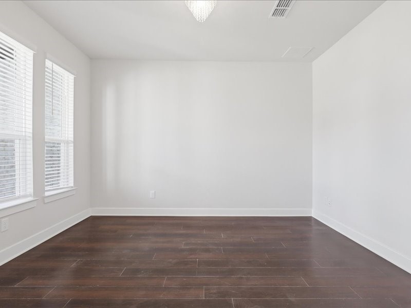 4710 Pecos Ridge Lane Sugar Land, TX 77479 - Photo 32 of 49 This photo shows a bright, empty room with dark hardwood floors and white walls. Large windows allow plenty of natural light, and a modern light fixture hangs from the ceiling.