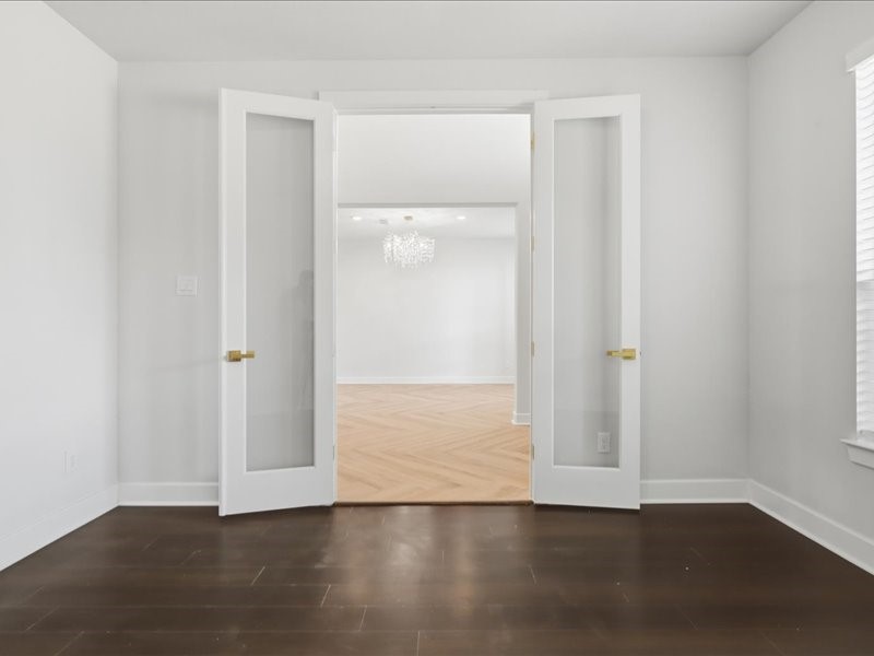 4710 Pecos Ridge Lane Sugar Land, TX 77479 - Photo 34 of 49 This photo showcases an elegant room with dark hardwood flooring and white walls. Double glass doors open into a bright space with a light wood floor and a modern chandelier, suggesting an inviting and stylish home.