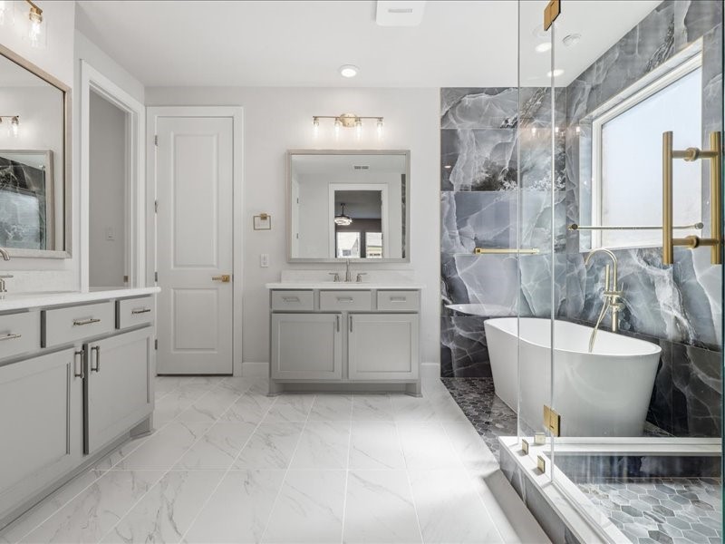 4710 Pecos Ridge Lane Sugar Land, TX 77479 - Photo 37 of 49 This modern bathroom features elegant gray cabinetry, a luxurious freestanding tub, and a sleek glass-enclosed shower. The marble-patterned tiles and large mirrors enhance the space's brightness, creating a spa-like atmosphere.