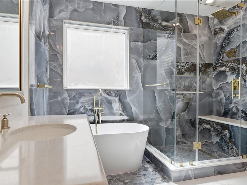 4710 Pecos Ridge Lane Sugar Land, TX 77479 - Photo 38 of 49 This luxurious bathroom features a freestanding tub, a spacious glass-enclosed shower, and stunning marble-patterned walls. The design is modern with elegant gold fixtures, creating a serene and sophisticated atmosphere.