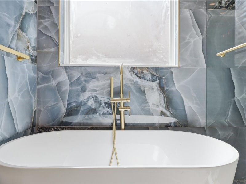 4710 Pecos Ridge Lane Sugar Land, TX 77479 - Photo 39 of 49 This bathroom features a luxurious freestanding tub with elegant gold fixtures, set against stunning marble-like blue wall tiles. A large window provides natural light, creating a serene and sophisticated atmosphere.