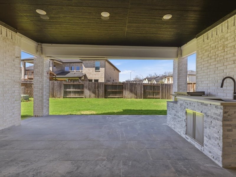 4710 Pecos Ridge Lane Sugar Land, TX 77479 - Photo 42 of 49 This photo showcases a covered outdoor patio with modern stone flooring and a built-in kitchenette. The area opens to a spacious, fenced backyard, ideal for entertaining and relaxation.