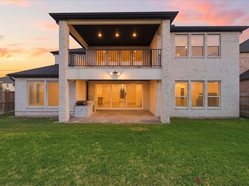 4710 Pecos Ridge Lane Sugar Land, TX 77479 - Photo 44 of 49 This photo showcases the back of a two-story home with a spacious covered patio, upper balcony, and large windows, offering a view of a well-maintained lawn and a beautiful sunset. Perfect for outdoor entertaining and relaxation.