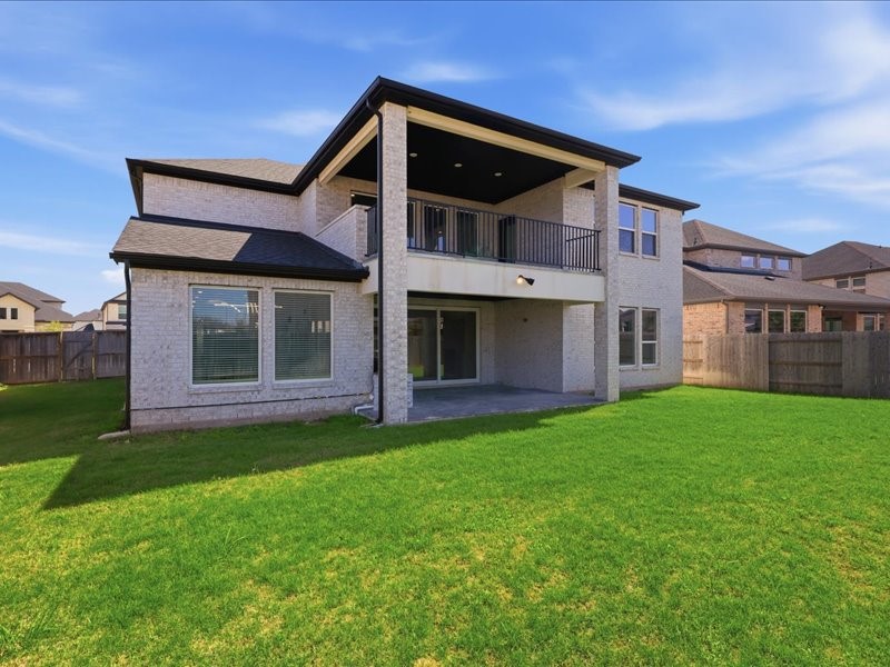 4710 Pecos Ridge Lane Sugar Land, TX 77479 - Photo 46 of 49 This photo shows the back of a two-story brick home with a covered patio and balcony, overlooking a spacious, well-maintained lawn. The yard is fenced, providing privacy and security.