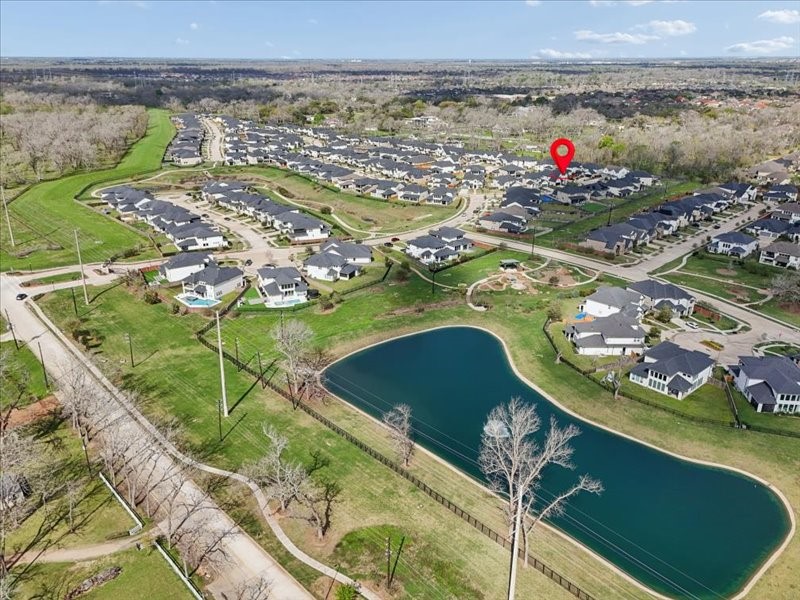 4710 Pecos Ridge Lane Sugar Land, TX 77479 - Photo 47 of 49 Aerial view of a suburban neighborhood featuring a large pond and lush green spaces. The area is neatly organized with modern homes, winding streets, and nearby wooded areas, offering a serene and picturesque environment.
