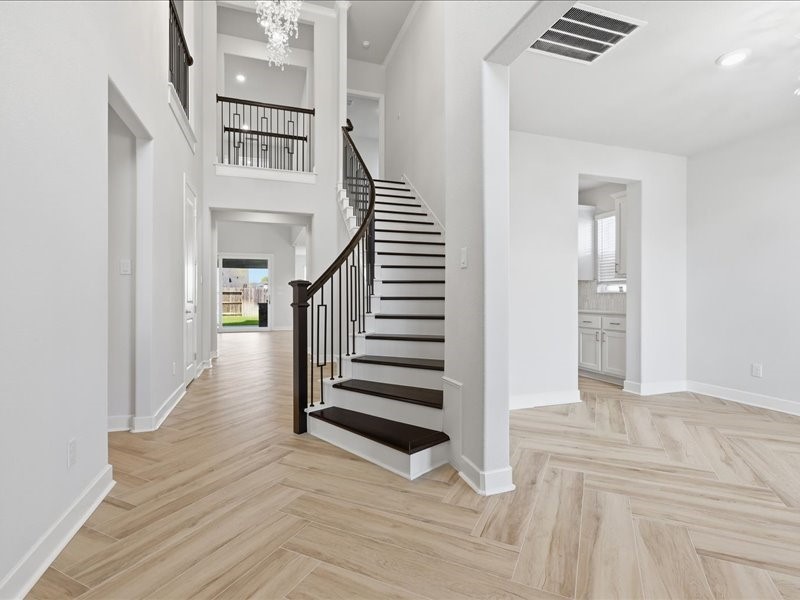 4710 Pecos Ridge Lane Sugar Land, TX 77479 - Photo 6 of 49 This photo showcases a bright, open foyer with elegant wood flooring, a grand staircase with dark wood accents, and high ceilings. The area leads to a kitchen and a living space with large windows, creating an inviting and spacious atmosphere.