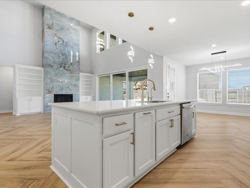 4710 Pecos Ridge Lane Sugar Land, TX 77479 - Photo 7 of 49 This photo showcases a spacious open-concept living area with a modern kitchen island featuring white cabinetry and elegant pendant lighting. The room is bright with large windows, wood-patterned flooring, and a stunning feature wall with built-in shelves and a fireplace.
