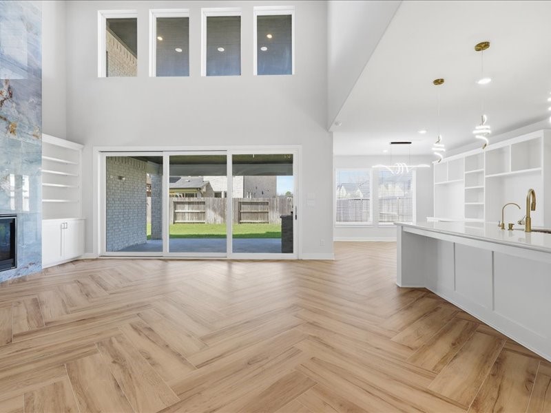 4710 Pecos Ridge Lane Sugar Land, TX 77479 - Photo 8 of 49 This spacious, modern living area features high ceilings, large windows for natural light, and sliding doors leading to a backyard. It includes an open-concept kitchen with elegant lighting, sleek cabinetry, and a stylish island. The wooden herringbone flooring adds warmth.