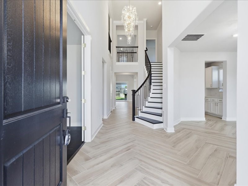 4710 Pecos Ridge Lane Sugar Land, TX 77479 - Photo 10 of 49 This photo showcases a bright and spacious entryway featuring a grand staircase, elegant chandelier, and sleek tile flooring, leading into an open-plan home with a modern aesthetic.