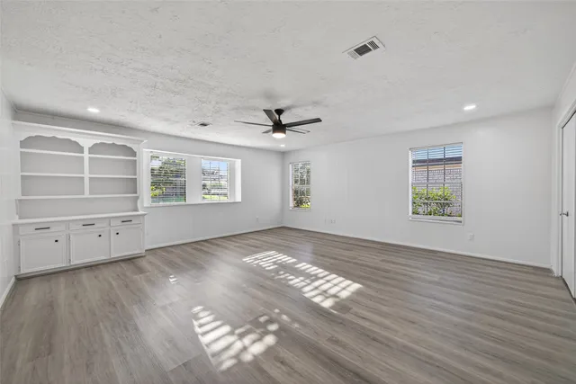 an empty room with wooden floor a ceiling fan a fireplace and windows