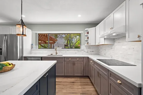 a kitchen with stainless steel appliances a sink dishwasher a refrigerator and white cabinets with wooden floor