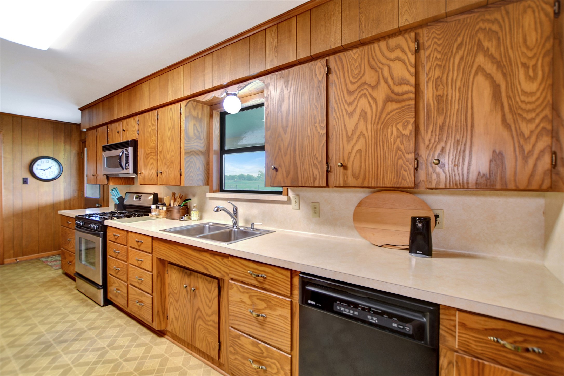 341 South S Loop Bellville, TX 77418 - Photo 13 of 33 This kitchen features warm wood cabinetry, a double sink, and modern appliances, including a stainless steel oven and microwave. A window provides natural light, complementing the spacious countertops.