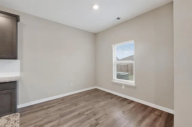 a view of an empty room with wooden floor and a window