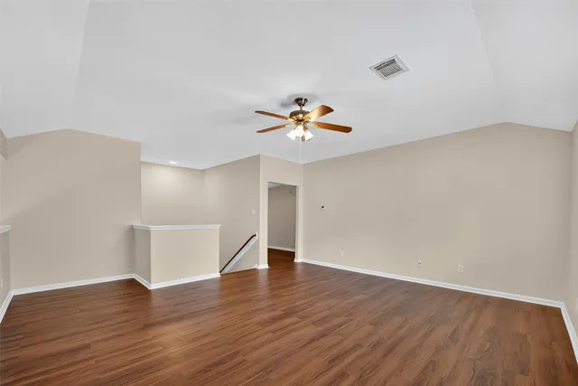 a view of an empty room with wooden floor and a ceiling fan