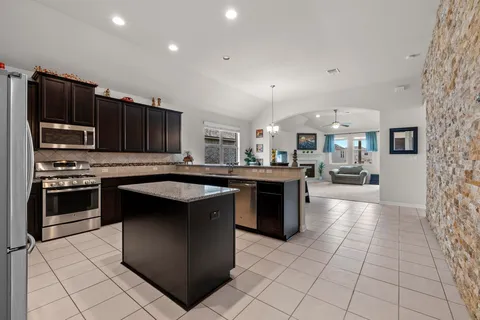 a kitchen with kitchen island granite countertop a stove top oven a sink dishwasher and cabinets