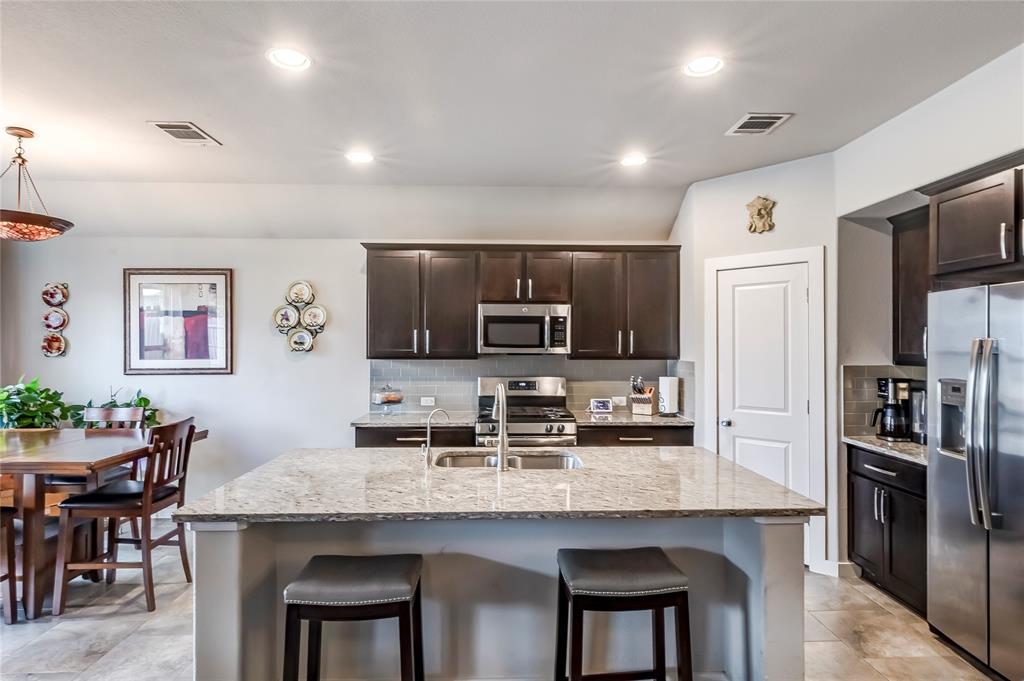 231 Windswept Way Kyle, TX 78640 - Photo 2 of 33 Kitchen featuring light stone countertops, stainless steel appliances, dark wood finish cabinets, an island with sink, and a kitchen breakfast bar