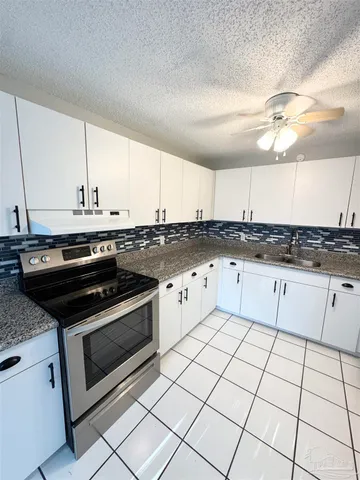 a white kitchen with granite countertop a stove top oven a sink dishwasher and a microwave oven on the counter