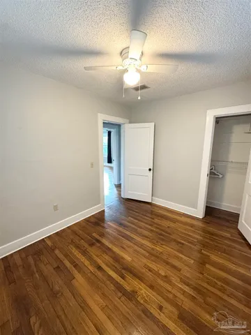 a view of an empty room with wooden floor and a ceiling fan