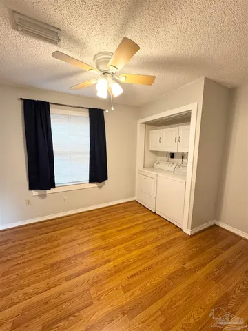 a view of an empty room with wooden floor and a ceiling fan
