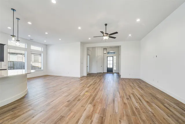 a view of an empty room with wooden floor and a kitchen