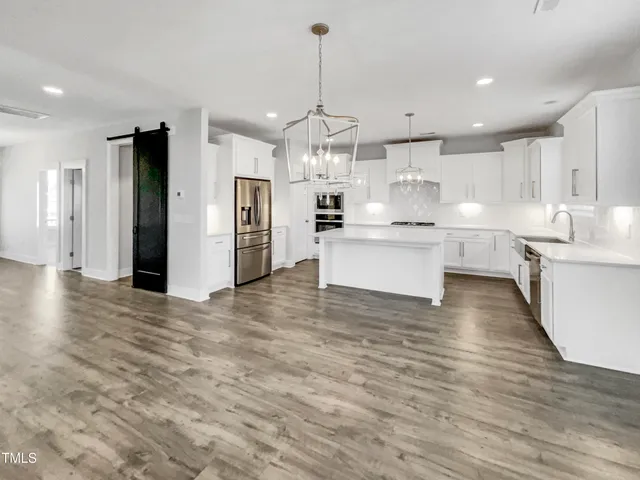 a kitchen with stainless steel appliances granite countertop a refrigerator oven a sink dishwasher and white cabinets with wooden floor