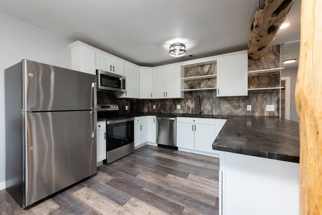 a kitchen with granite countertop a refrigerator a sink and white cabinets