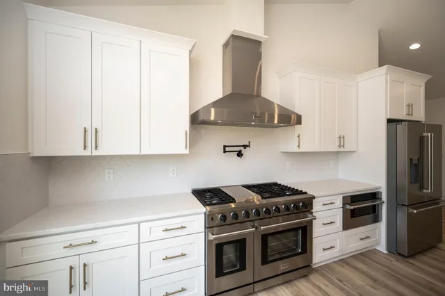 a kitchen with stainless steel appliances a refrigerator a sink dishwasher a stove and white cabinets with wooden floor