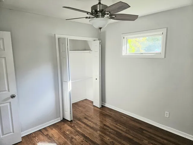 an empty room with wooden floor closet and windows